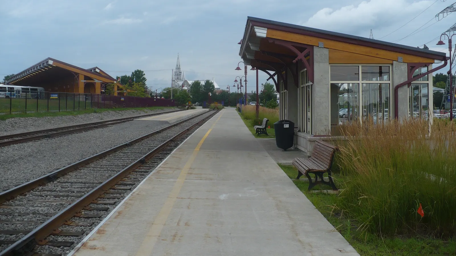 Quai de la gare de Saint-Jérôme avec voies ferrées, abri vitré et clocher d'église à l'arrière-plan